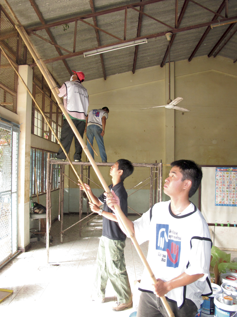 Four men in Mormon Helping Hands shirts painting with long poles inside a building in Thailand.
