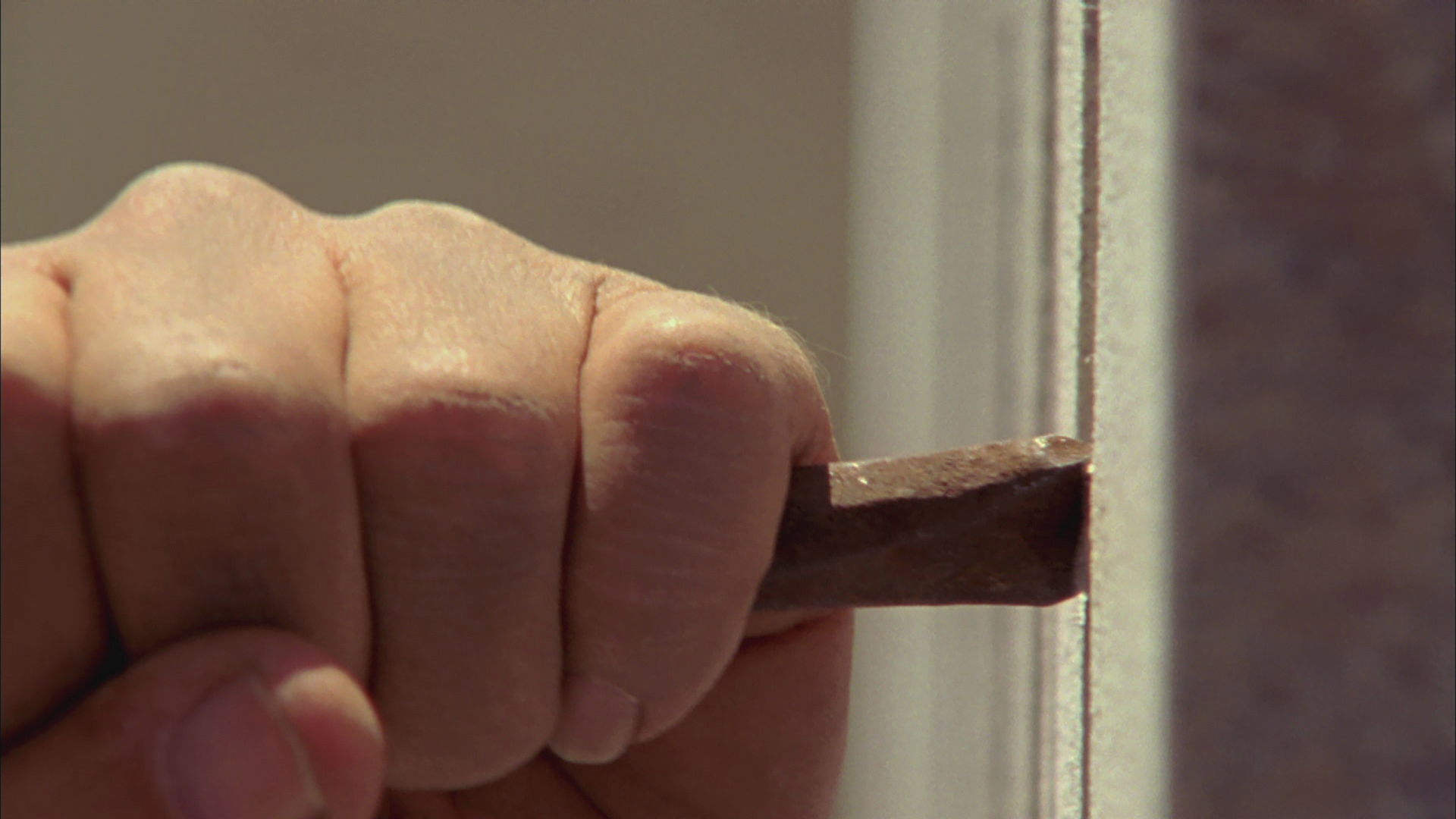 An image of a hand holding on to an iron rod pressing against stone.