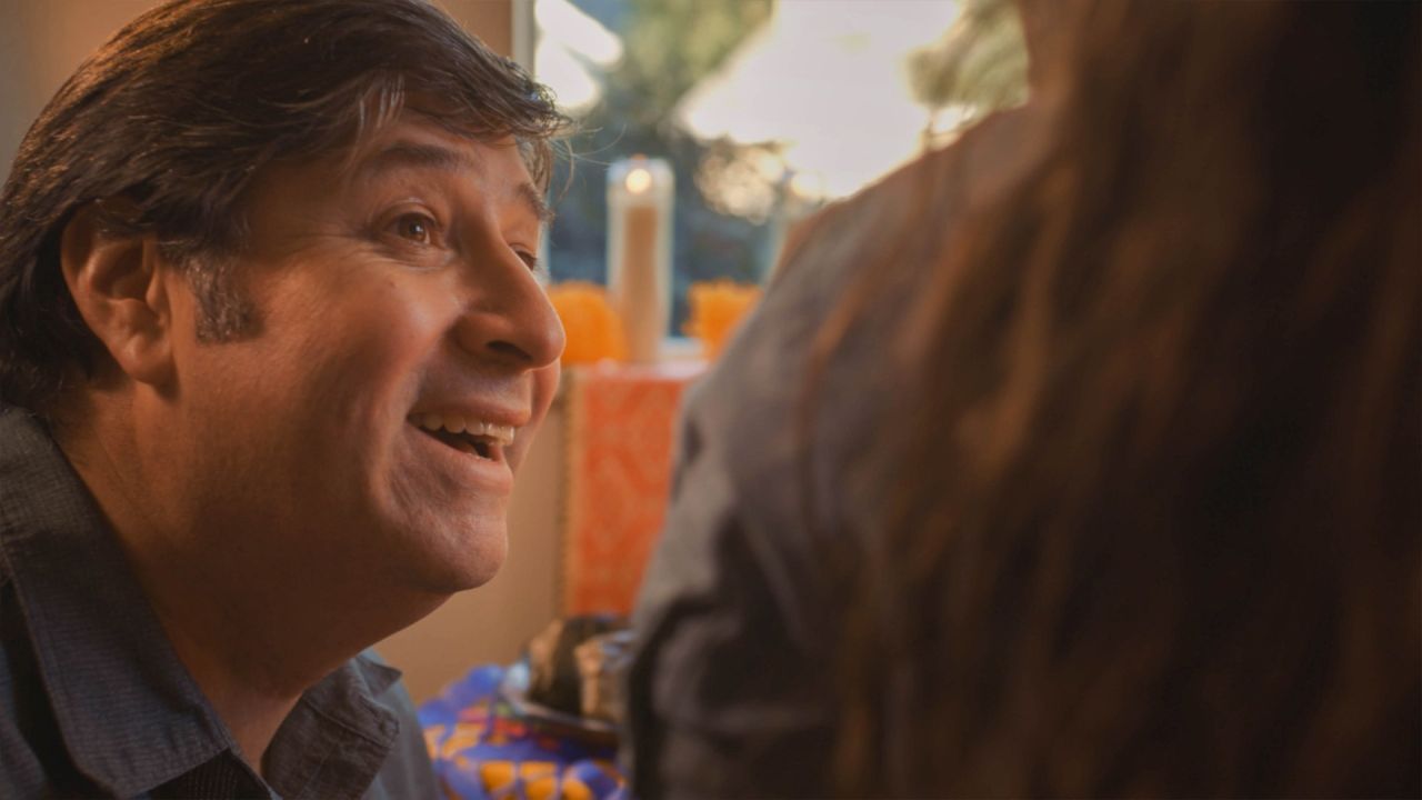 Un hombre honra la vida de su madre celebrando el Día de los Muertos junto a su familia.
