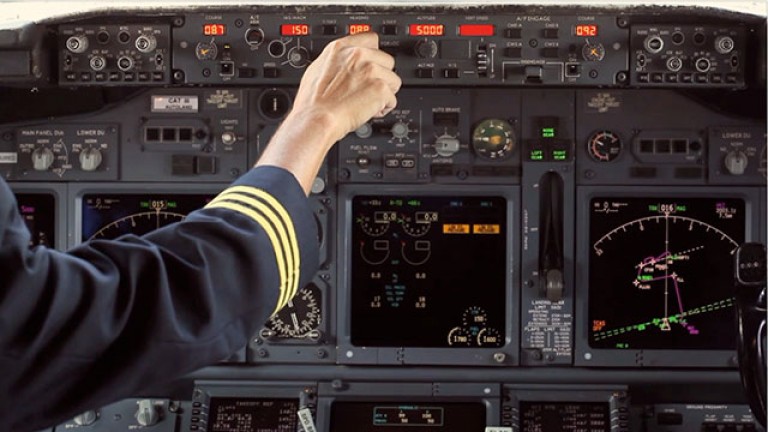 A photo of airplane controls with a pilots hand pushing a button.