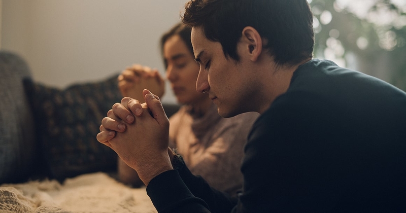 A couple kneel in prayer at their bed together