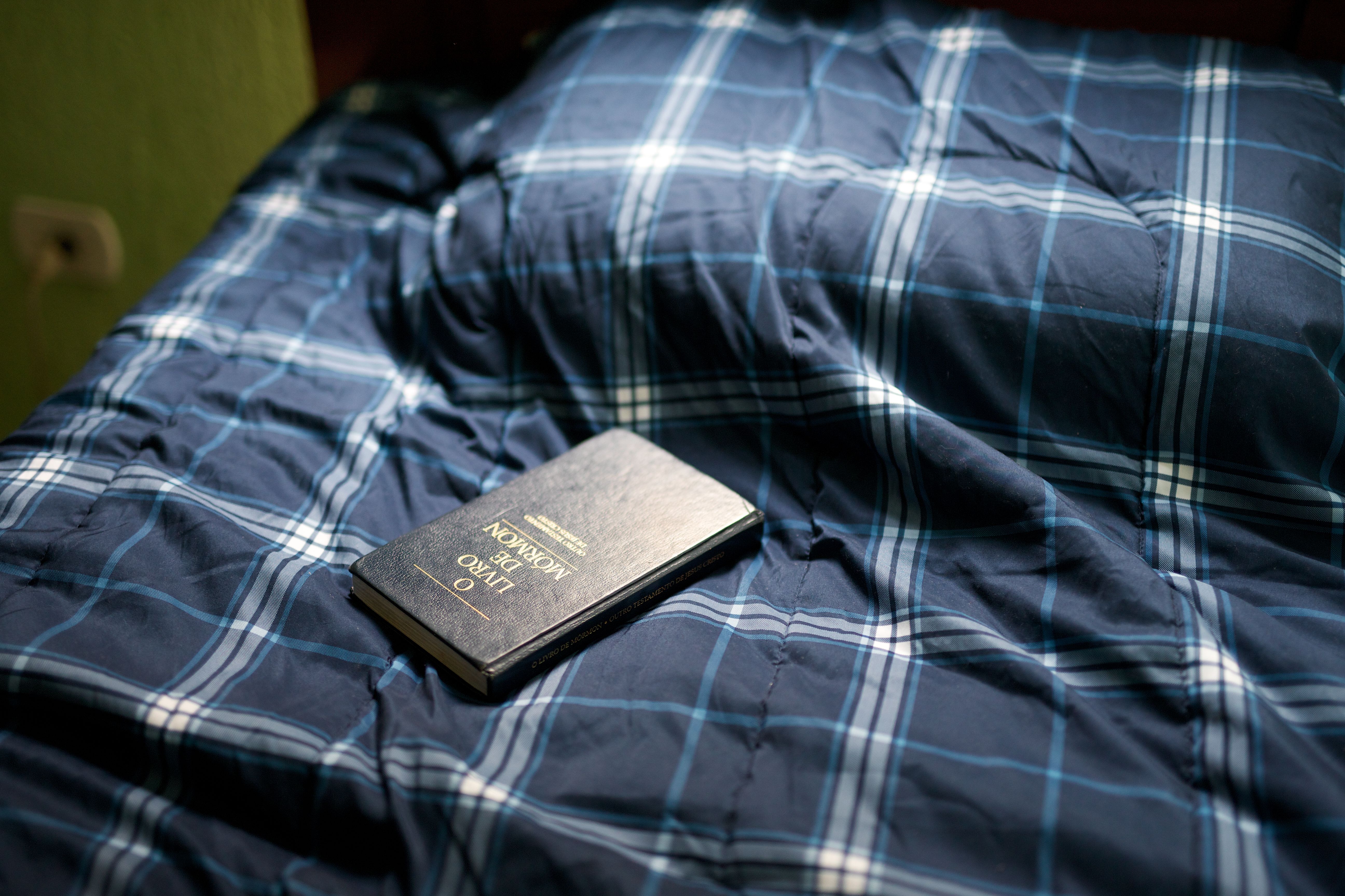 A Portuguese copy of the Book of Mormon lying closed on a bed.