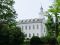 A side view of the Kirtland Temple, surrounded by large green trees and bushes.