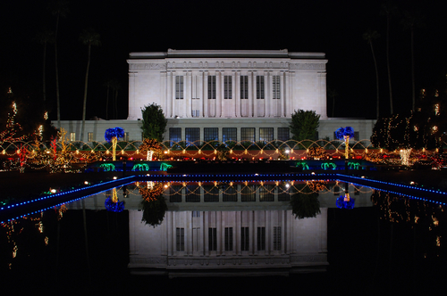 The Mesa Arizona Temple is seen reflected in a pool of water, surrounded by Christmas lights at night.