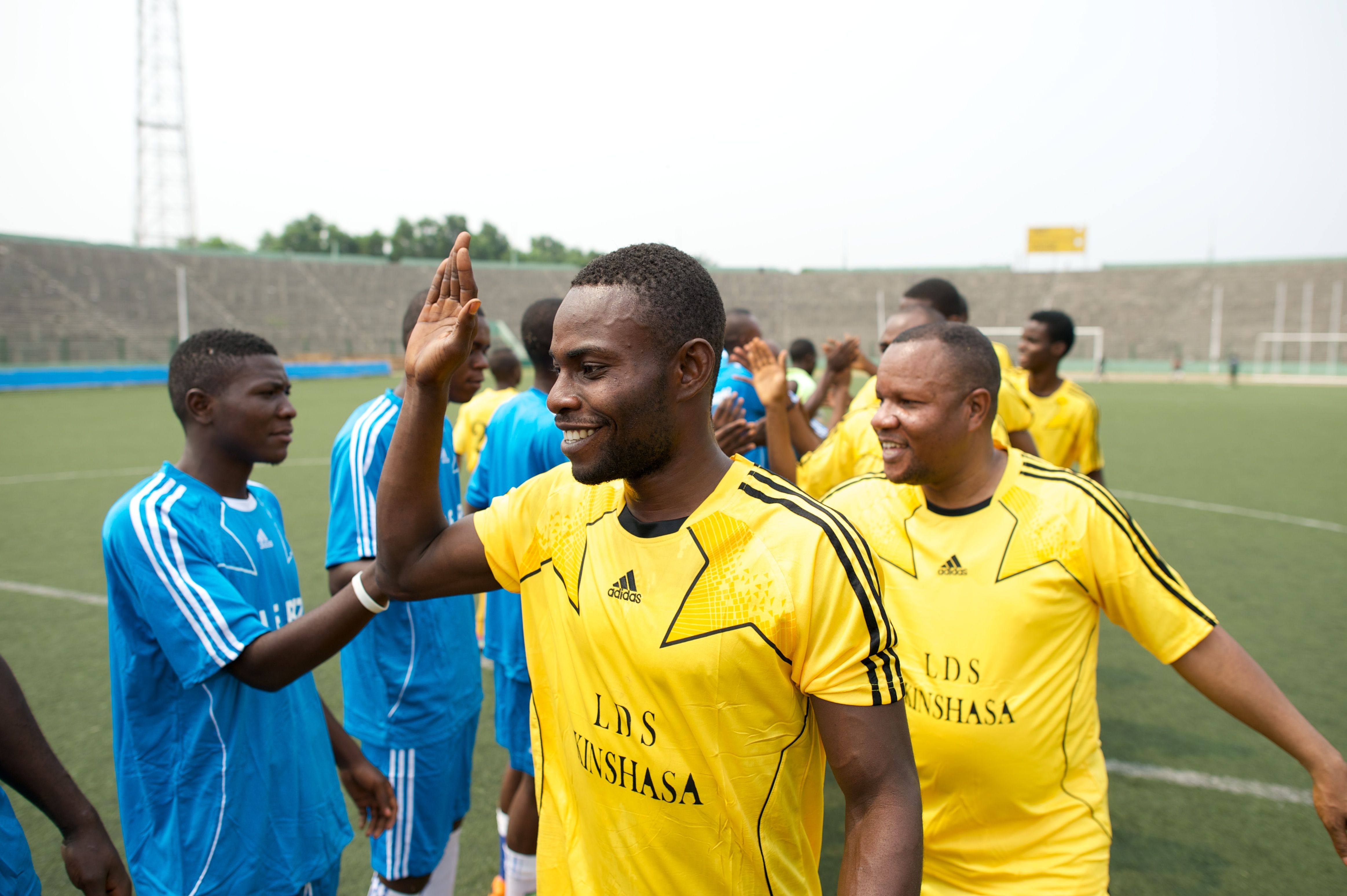 Men from Africa walk in two lines, giving high fives to the opposite team at a soccer game.