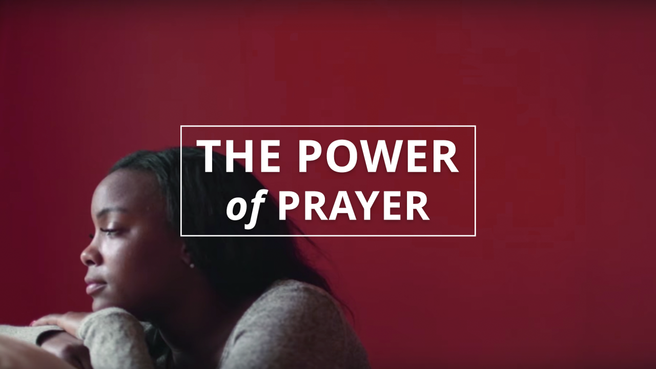 A woman kneels in prayer at her bed