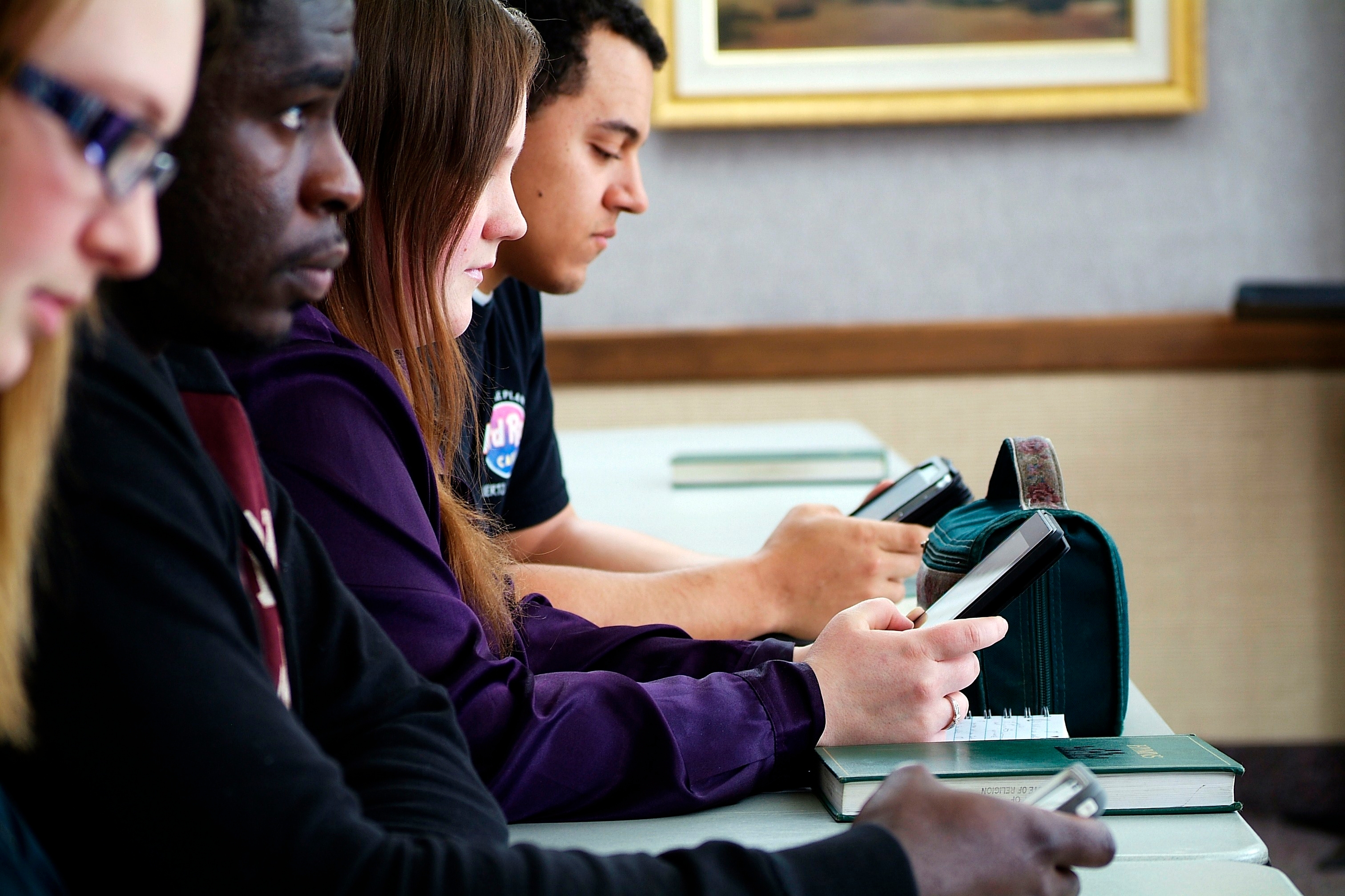 A group of teenagers look at their smartphones while sitting at a table in seminary.