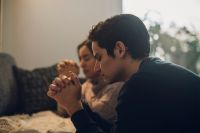A couple kneel in prayer at their bedside