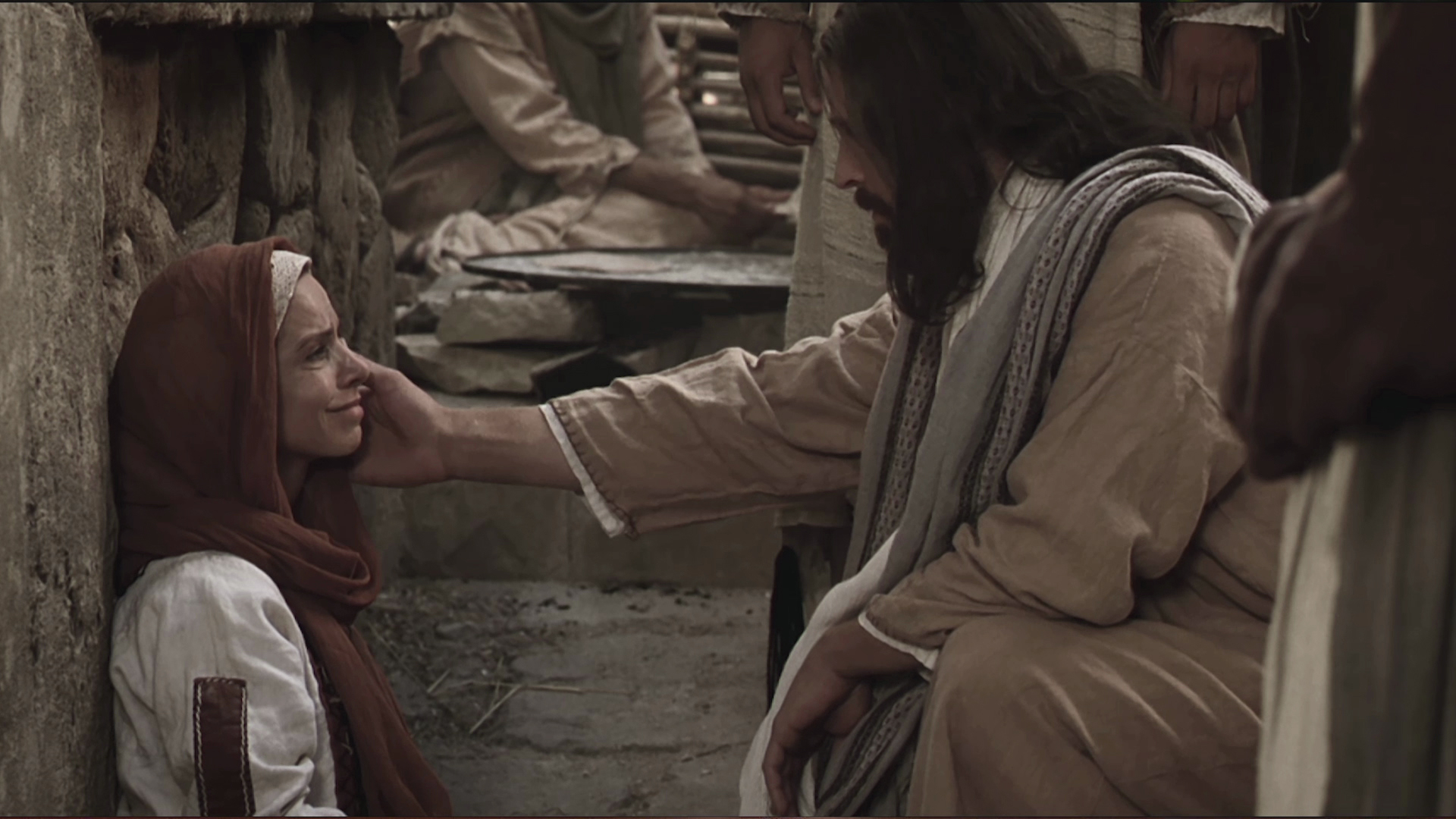 A photo of Jesus Christ kneeling before a woman sitting on the ground with his hand stretched out.