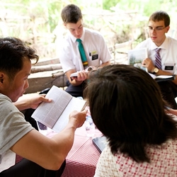 Two elder missionaries teach a family about the gospel of Jesus Christ in their living room