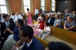 A mother and her daughters sit on a chapel pew greeting other members of the congregation