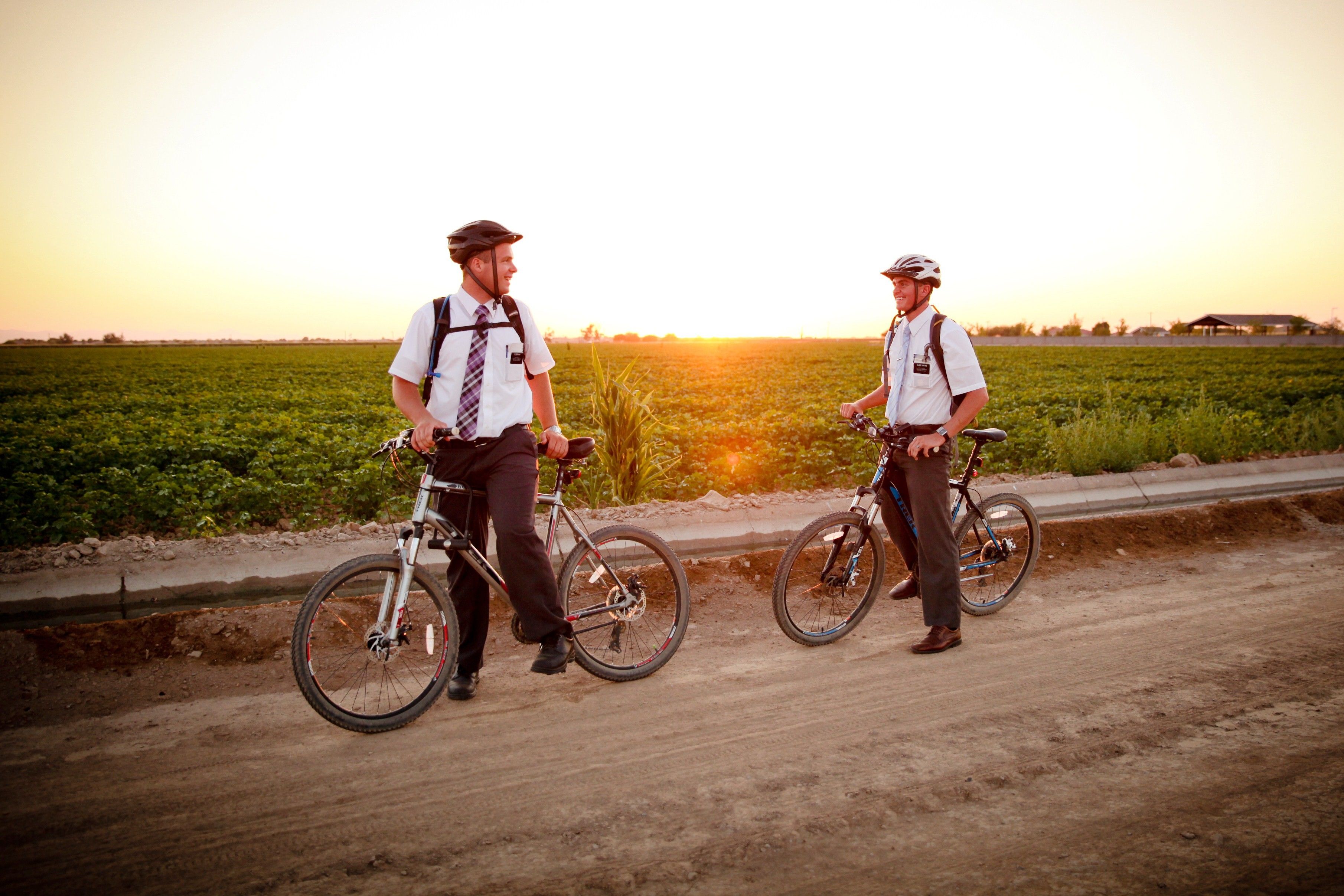 Two elder missionaries stand with their bikes next to a field.