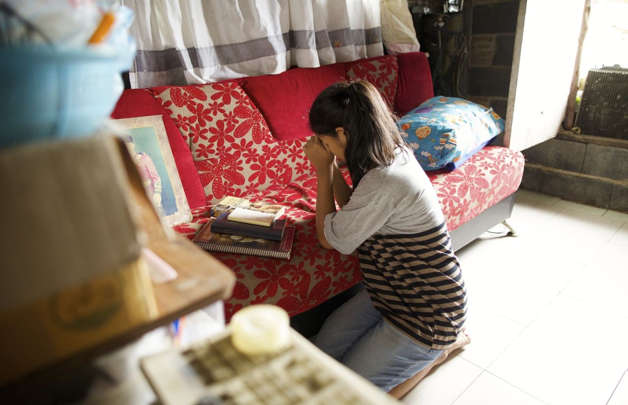 A young woman kneels in prayer in her living room asking God to please help her