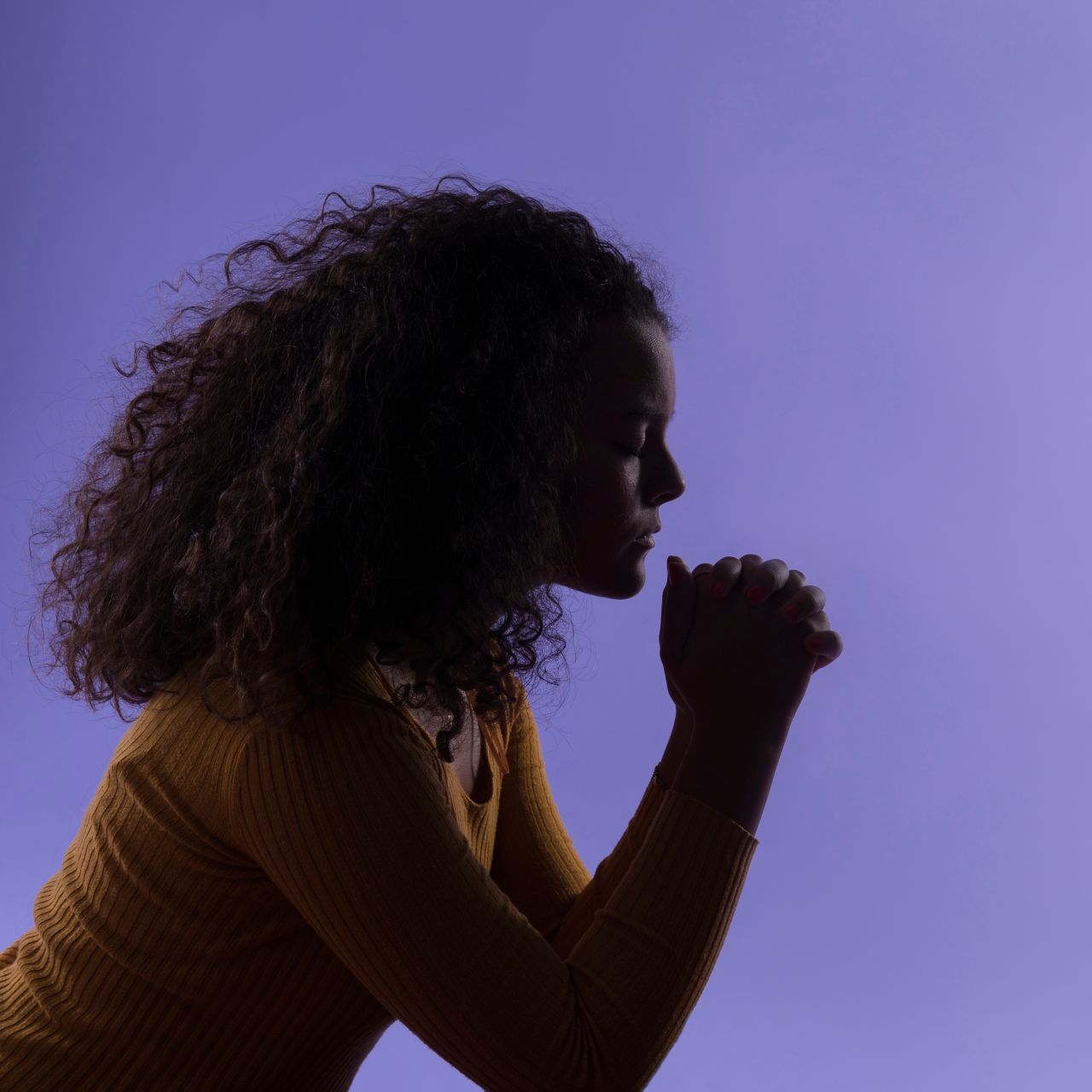 A woman kneels in prayer at her bed