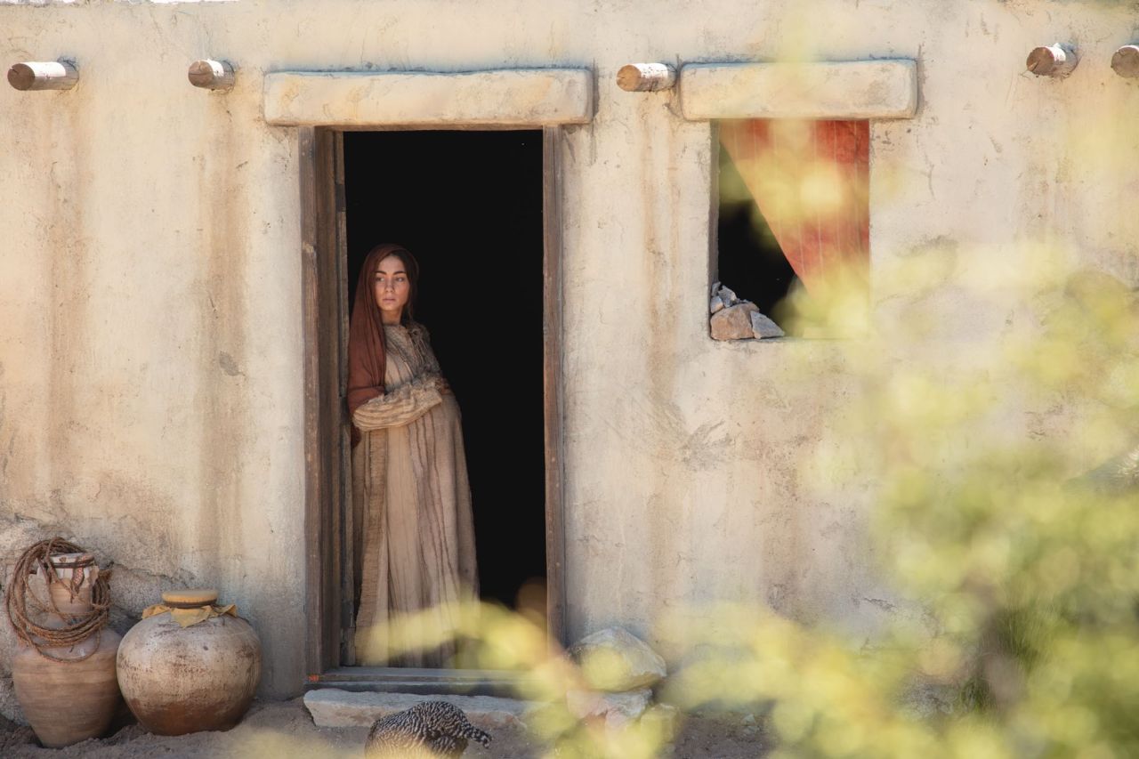 A pregnant Mary, the mother of Jesus stands in a door way