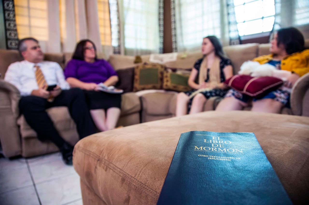 Una familia sentada en su casa, con el Libro de Mormón