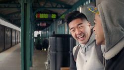 Two men sit together on a bench in a train station enjoying each others company