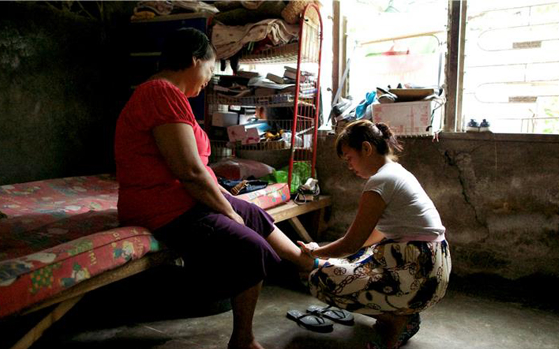 A daughter preforms service for her elderly mother helping to put her shoes on