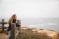 A woman overlooking the sea leans against a railing contemplating teachings of Jesus Christ
