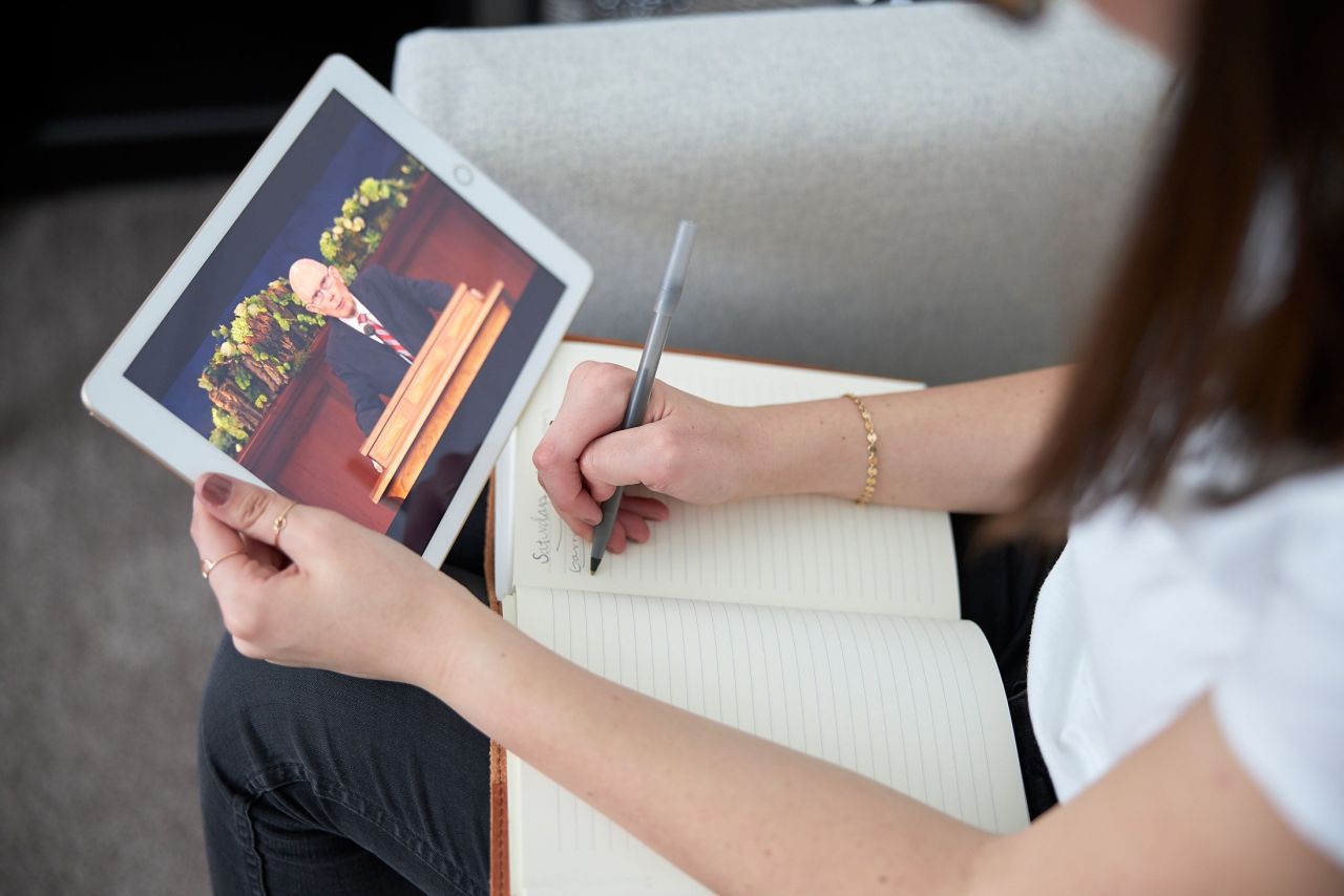 A woman watching General Conference on a tablet while taking notes