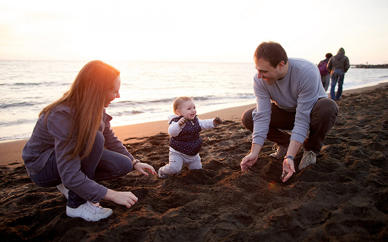 A young couple play on the sand at the beach with their baby