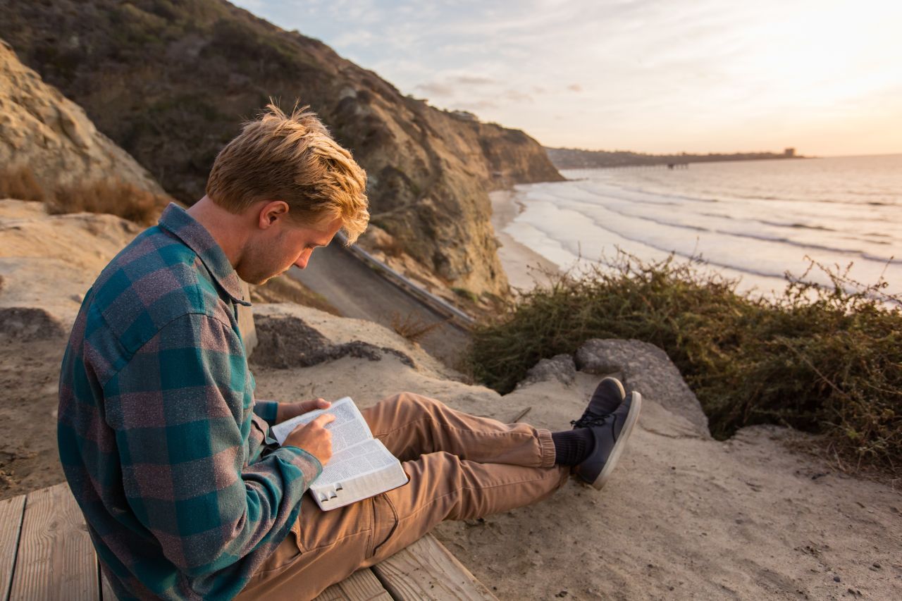 A man sits at the beach studying the Book of Mormon