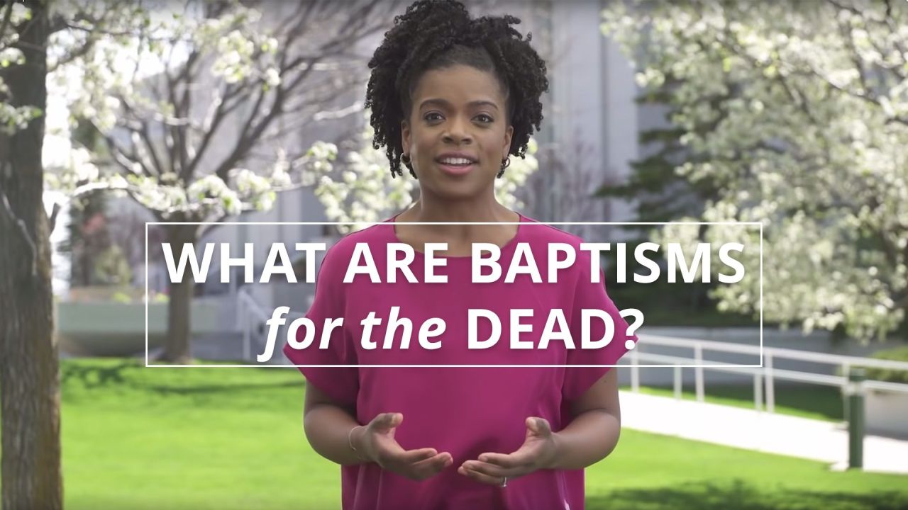 A woman stands smiling in front of temple during spring to explain why baptisms for the dead are preformed in temples