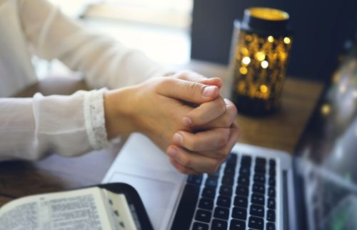 Woman's hands by computer in attitude of prayer
