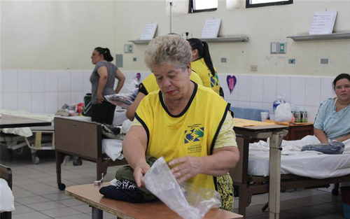 An elderly woman helps do service in a temporary shelter unpacking clean clothes