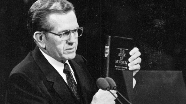 President Packer holds a Book of Mormon at the pulpit