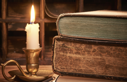 A pile of two thick,old books next to a candle